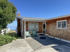 A coastal house with a patio, two chairs, a small table, and a welcome sign.
