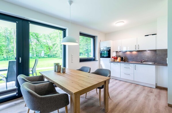 A modern kitchen with white cabinets, a wooden dining table, and a large window. - Vacation apartment "Mooswinkel" with terrace on Lake Krakow (Krakow am See)