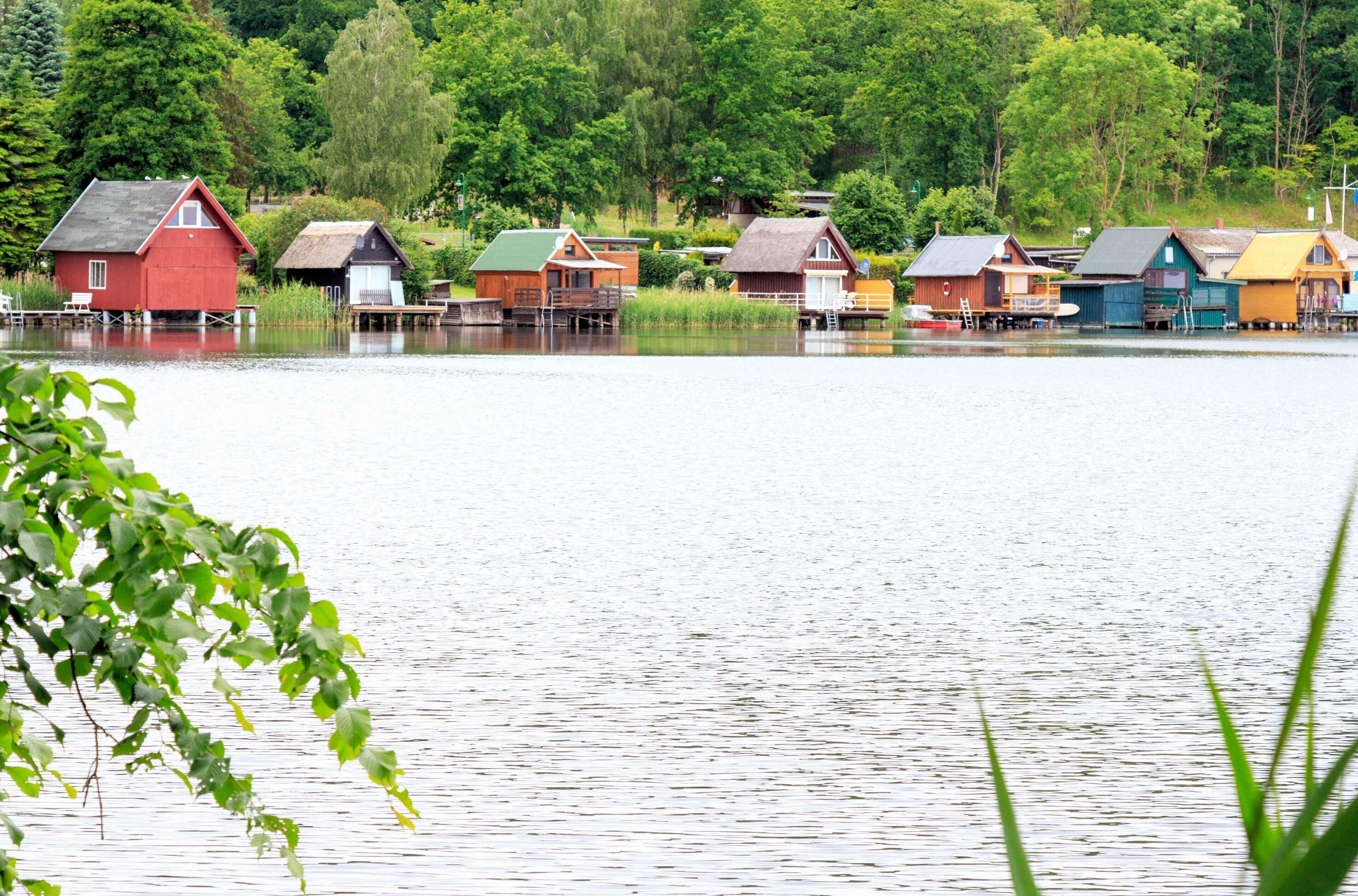 Una hilera de casas de madera coloridas sobre pilotes, junto a un lago tranquilo, rodeadas de exuberante vegetación.