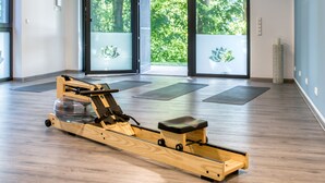 A rowing machine in a room with large windows, wooden flooring, and exercise mats. - Vacation apartment "Silberreiher" with balcony in Krakow am See (Krakow am See)