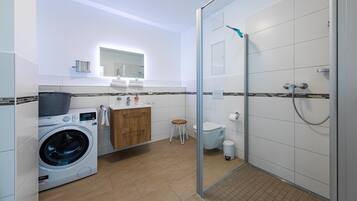 A modern bathroom with a glass-enclosed shower, a washing machine, a sink with a mirror, and a toilet.