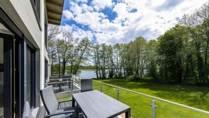 A balcony with a table and chairs overlooking a lake and trees. - 5 star vacation apartment "Frau Hummel" on Lake Krakow (Krakow am See)