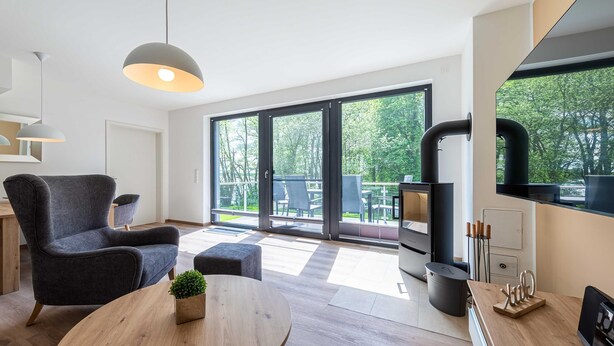 Un salón moderno con un sillón gris oscuro, una mesa redonda de madera con una planta y un ventanal con vistas al exterior.