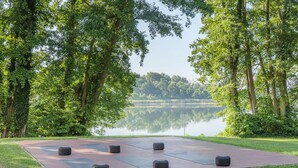 Un parque con zona pavimentada, árboles y un lago.