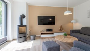 Una sala de estar moderna con una estufa de leña empotrada, un televisor de pantalla plana, un sofá gris y una mesa de centro redonda.