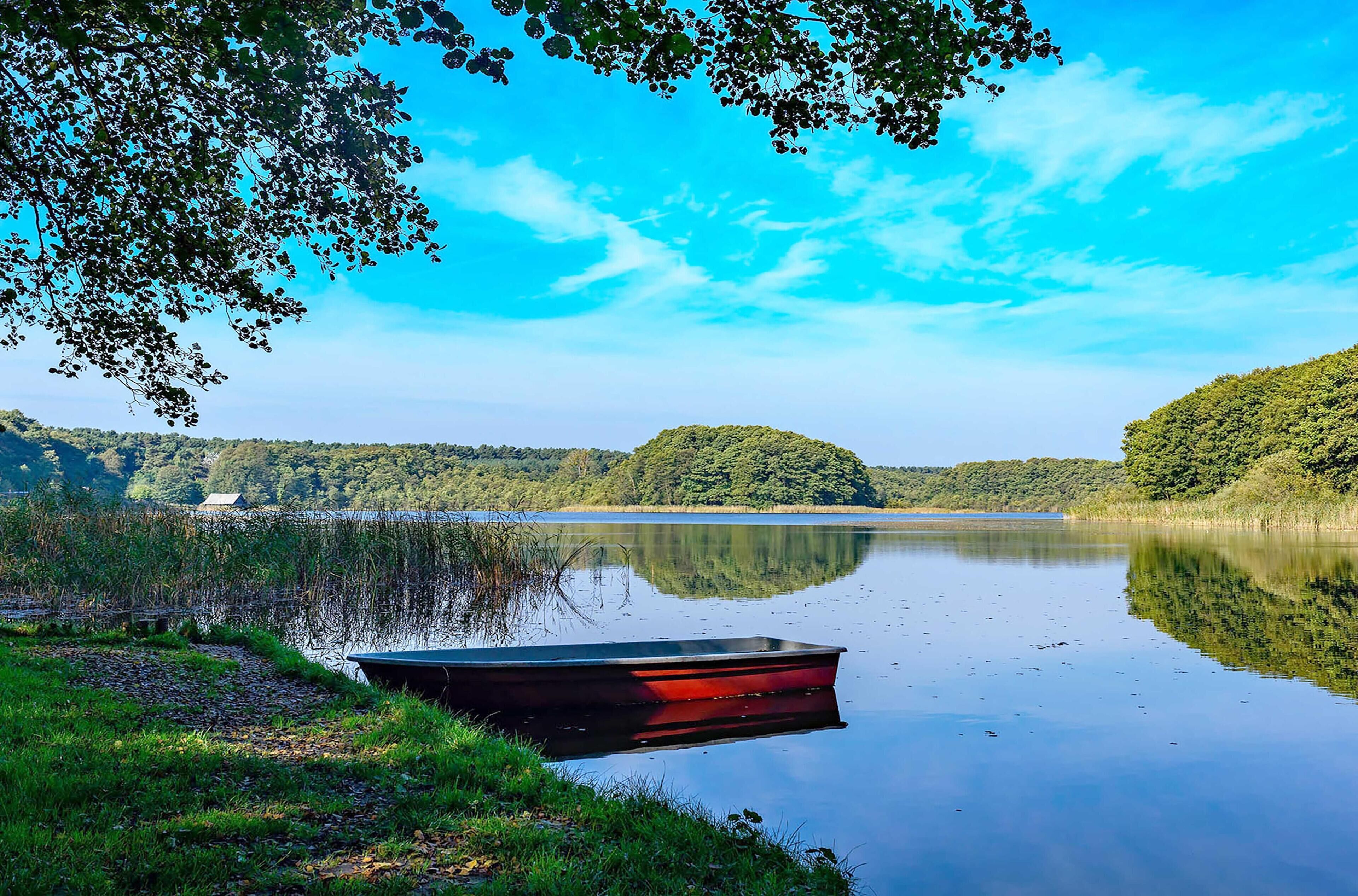 Een rustig meer met een boot aan de oever, omgeven door weelderige begroeiing en heuvels.