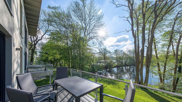 Una terraza con mesa y sillas que da a un lago y árboles.