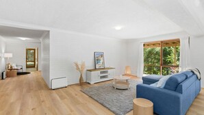 A modern living room with a blue sofa, a white entertainment unit, and a large window with a view of greenery.