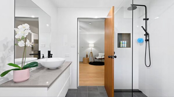 A modern bathroom with a white sink, a large mirror, and a shower. - Lilli Pilli Beach Retreat (Lilli Pilli)