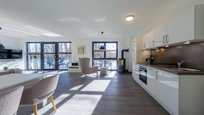 Une cuisine moderne avec des meubles blancs, une grande fenĂŞtre et un coin repas comprenant une table et des chaises blanches.