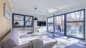 Un salon moderne avec un canapé, un téléviseur et un balcon aménagé avec du mobilier d’extérieur.
