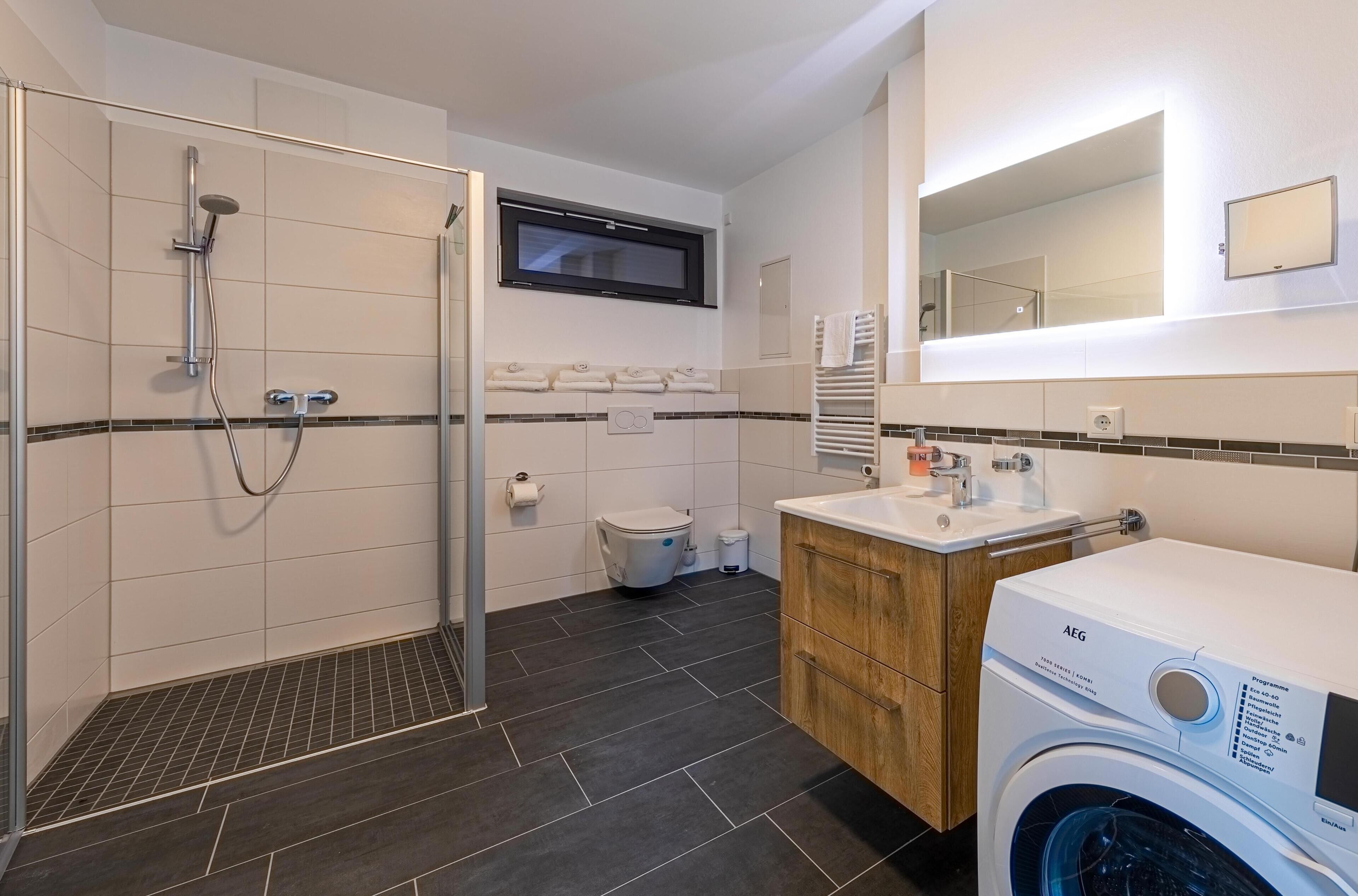 Een moderne badkamer met een douche, toilet en een wasmachine.
