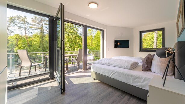 Et moderne soveværelse med en stor seng, et sengebord og udsigt til en balkon med havemøbler.