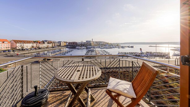 Eine Terrasse mit Tisch und Stuhl mit Blick auf einen Yachthafen, in dem Boote und Gebäude liegen.