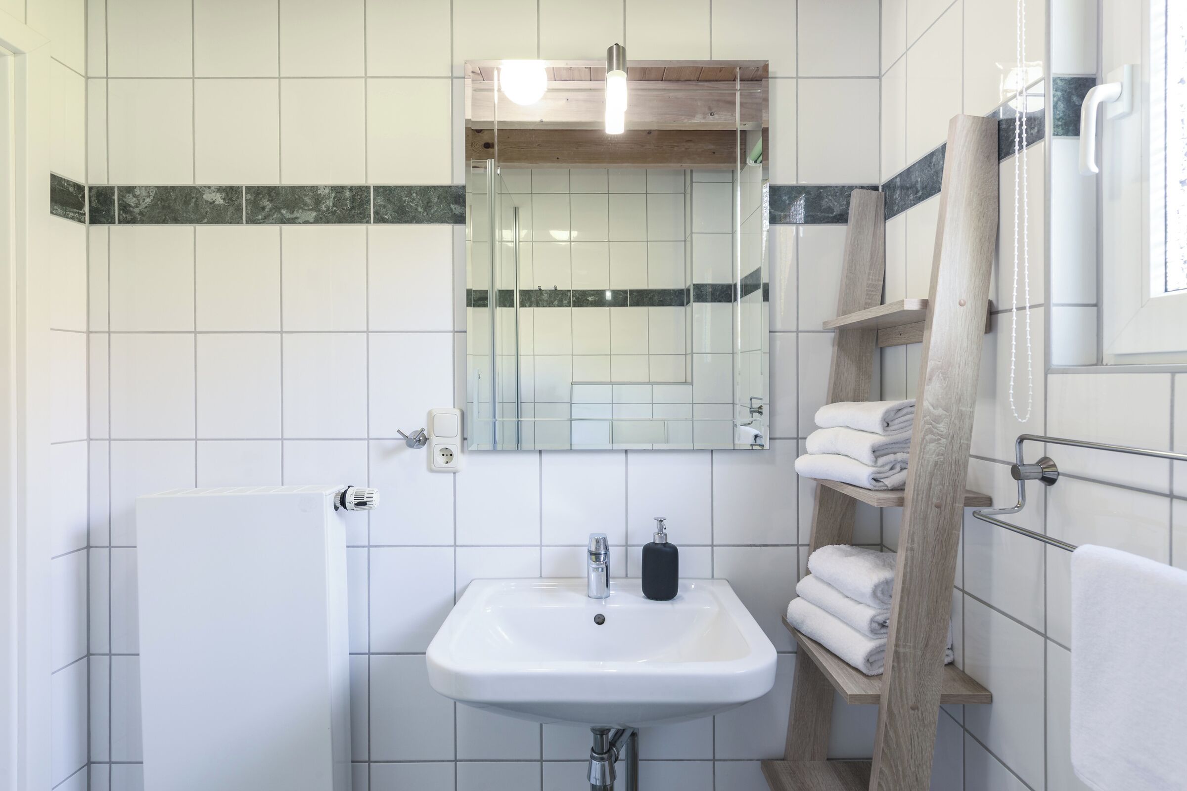 Une salle de bain avec un lavabo blanc, un miroir, un porte-serviettes et un espace douche.