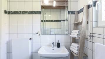Une salle de bain avec un lavabo blanc, un miroir, un porte-serviettes et un espace douche.