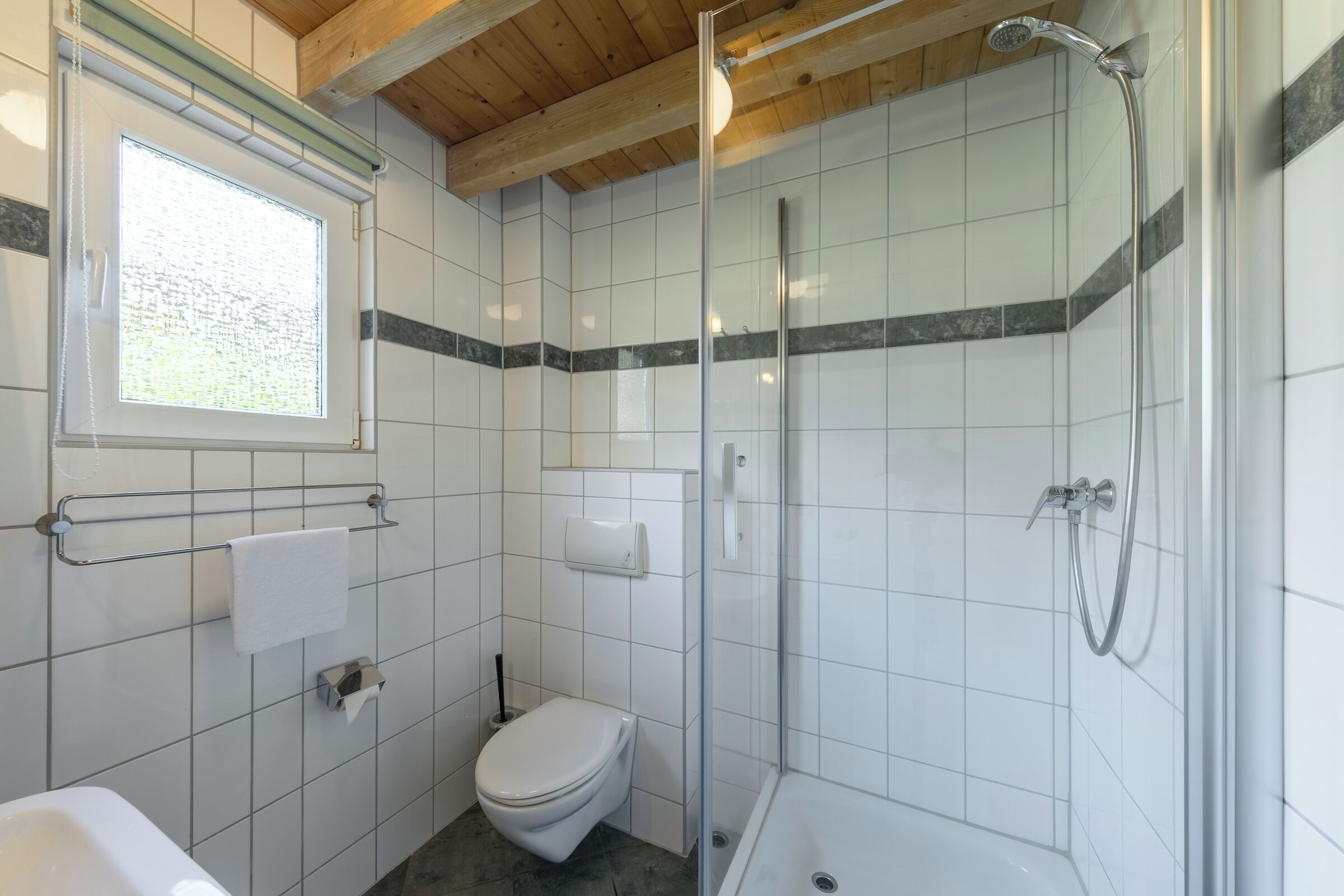 Et badeværelse med et brusebadekar i glas, toilet, vask og et vindue.