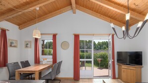 A spacious room with a wooden ceiling, a dining table with chairs, a TV, and a sliding glass door leading to an outdoor area. - "Sonnenschein" Vacation Home on Lake Jabelschen (Jabel)