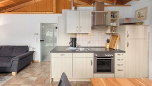 A modern kitchen with wooden cabinets, a built-in oven, and a dining area with a wooden table. - "Sonnenschein" Vacation Home on Lake Jabelschen (Jabel)