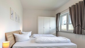 A bedroom with a wooden headboard, white bedding, a bedside lamp, a wardrobe, and a window with curtains.