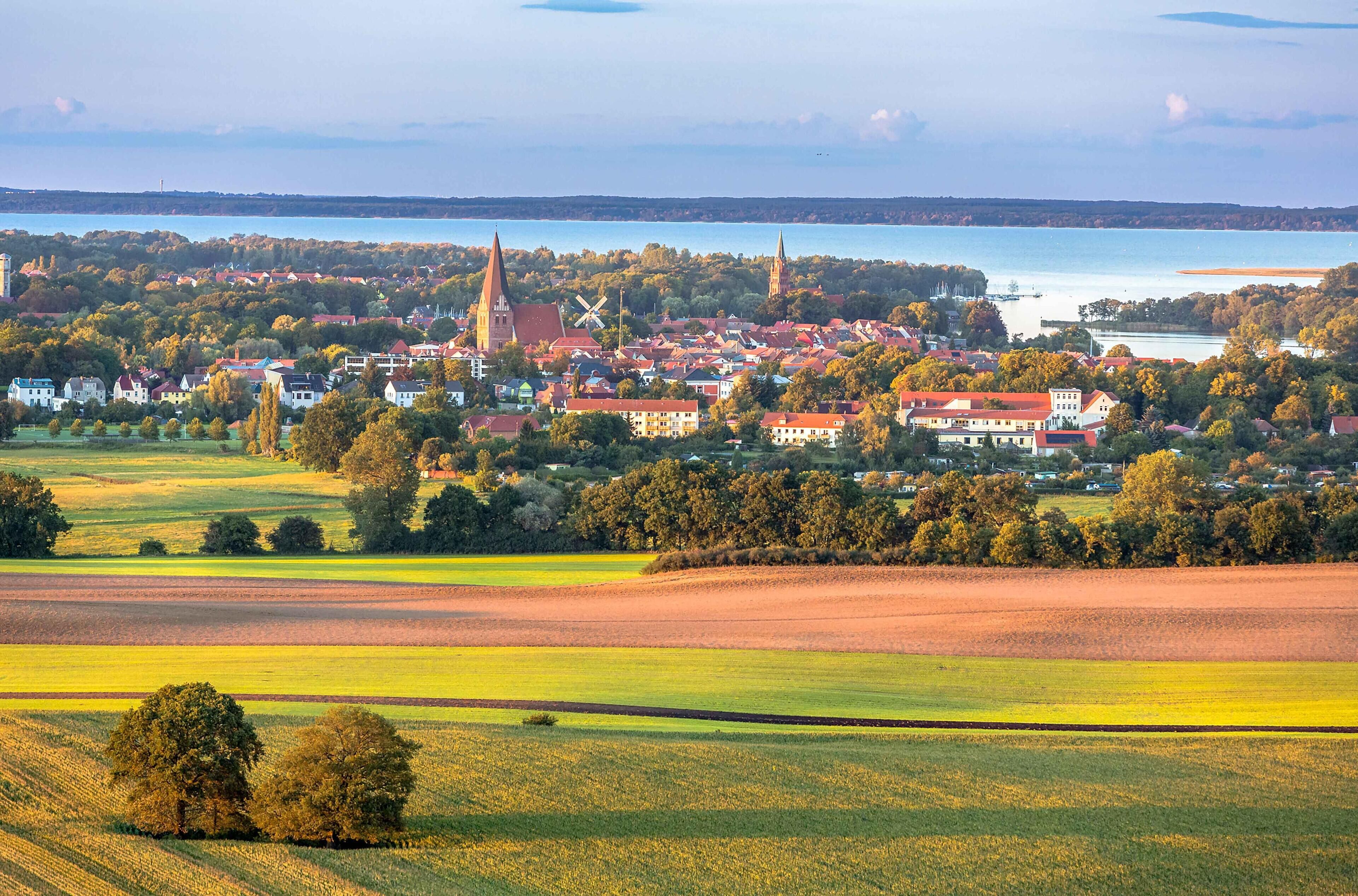 Eine Stadt mit einer markanten Kirche und einem Windrad, umgeben von Feldern und einem See.