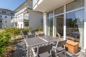 Une terrasse extérieure moderne, aménagée avec une table et des chaises, un banc en bois et une porte vitrée donnant sur un balcon.