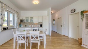 A modern kitchen with white cabinets, a dining table with chairs, and a wooden floor.
