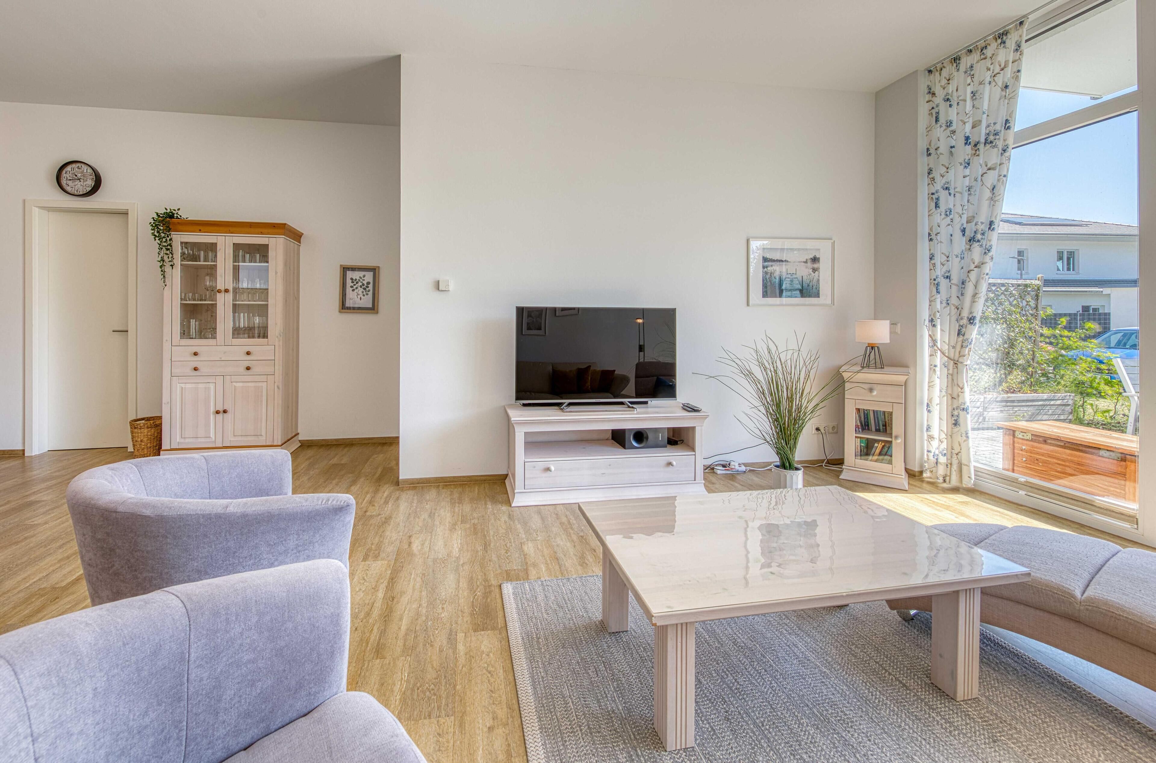 Una sala de estar moderna con un televisor de pantalla plana, sofás grises, una mesa de centro y un amplio ventanal con cortinas.