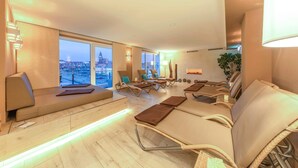 Un área de estar moderna con diversas opciones de asientos, incluyendo sofás y sillones, dispuesta alrededor de un espacio central con vistas a la ciudad.