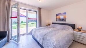 Un dormitorio con cama, mesita de noche, lámpara, ventana con cortinas y vista a un edificio.
