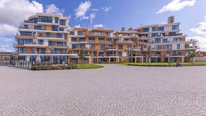 A modern multi-story building with a courtyard, featuring a mix of brick and glass facades, and a paved open area with umbrellas. - 4-star apartment Sieglinde in the harbor residence. (Waren (Müritz))