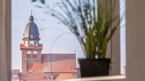 A view of a building with a prominent dome and clock tower through a window, with a potted plant in the foreground. - 4-star apartment Sieglinde in the harbor residence. (Waren (Müritz))