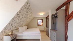 A bedroom with a sloped ceiling, a bed, a dresser, and a TV.