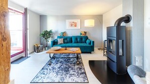 A modern living room with a teal sofa, a wooden coffee table, a black fireplace, and a large window.
