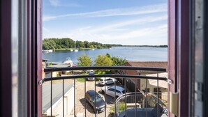 A balcony with a view of a lake, parked cars, and a building in the background.
