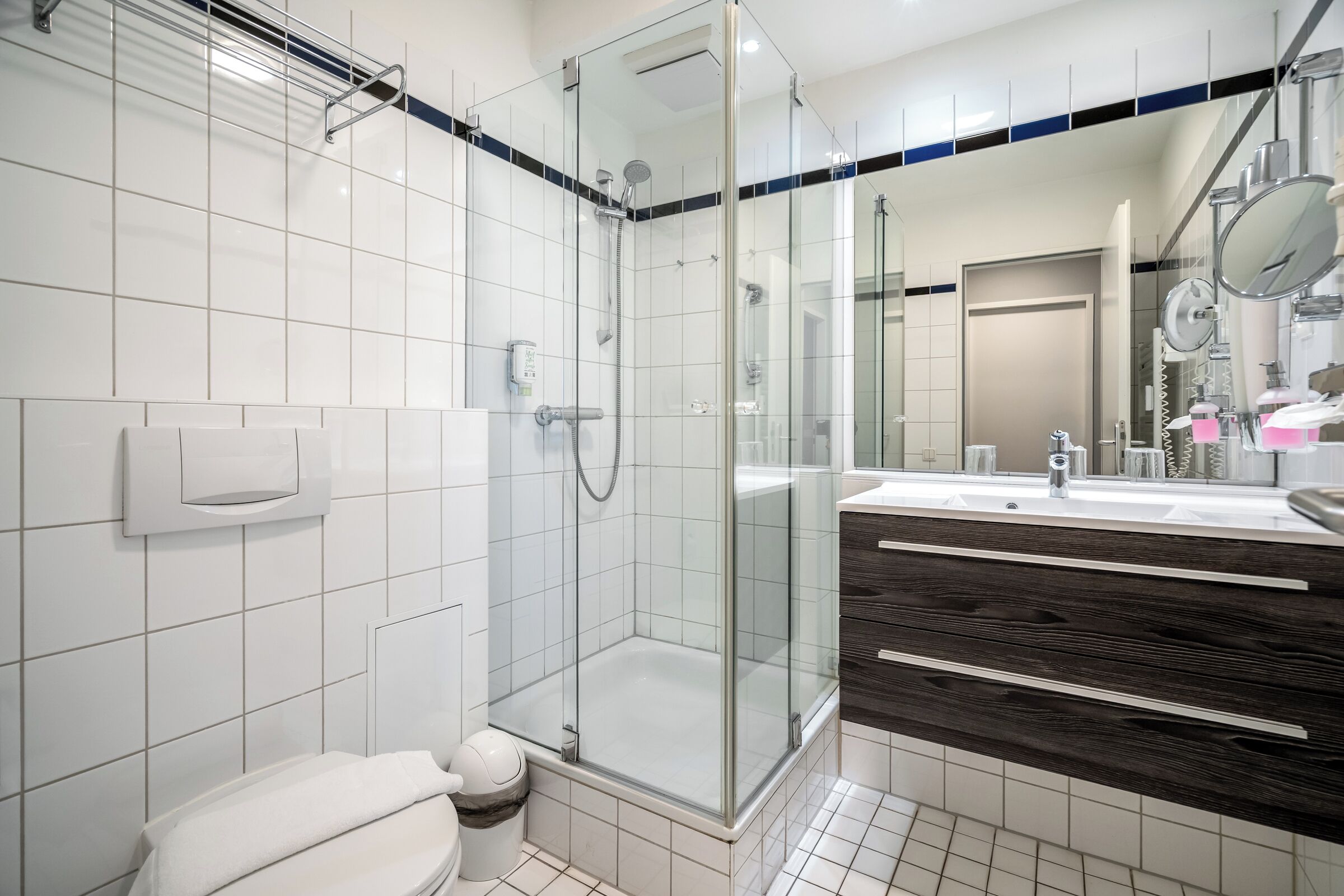 Et moderne badeværelse med bruseniche i glas, toilet, vaskebord med spejl og håndvask.