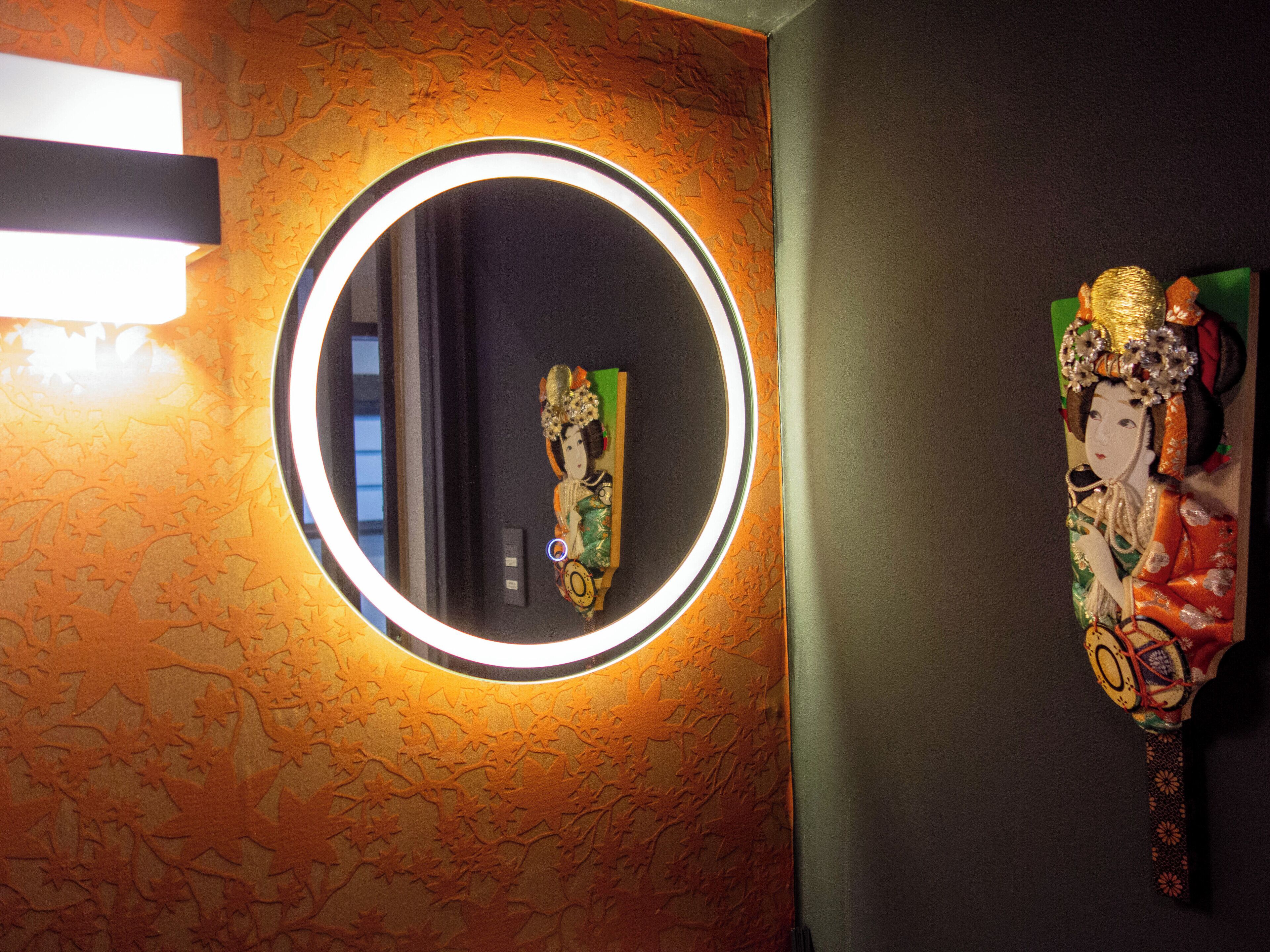 A bathroom with a round mirror, a wall-mounted light, and a decorative item.