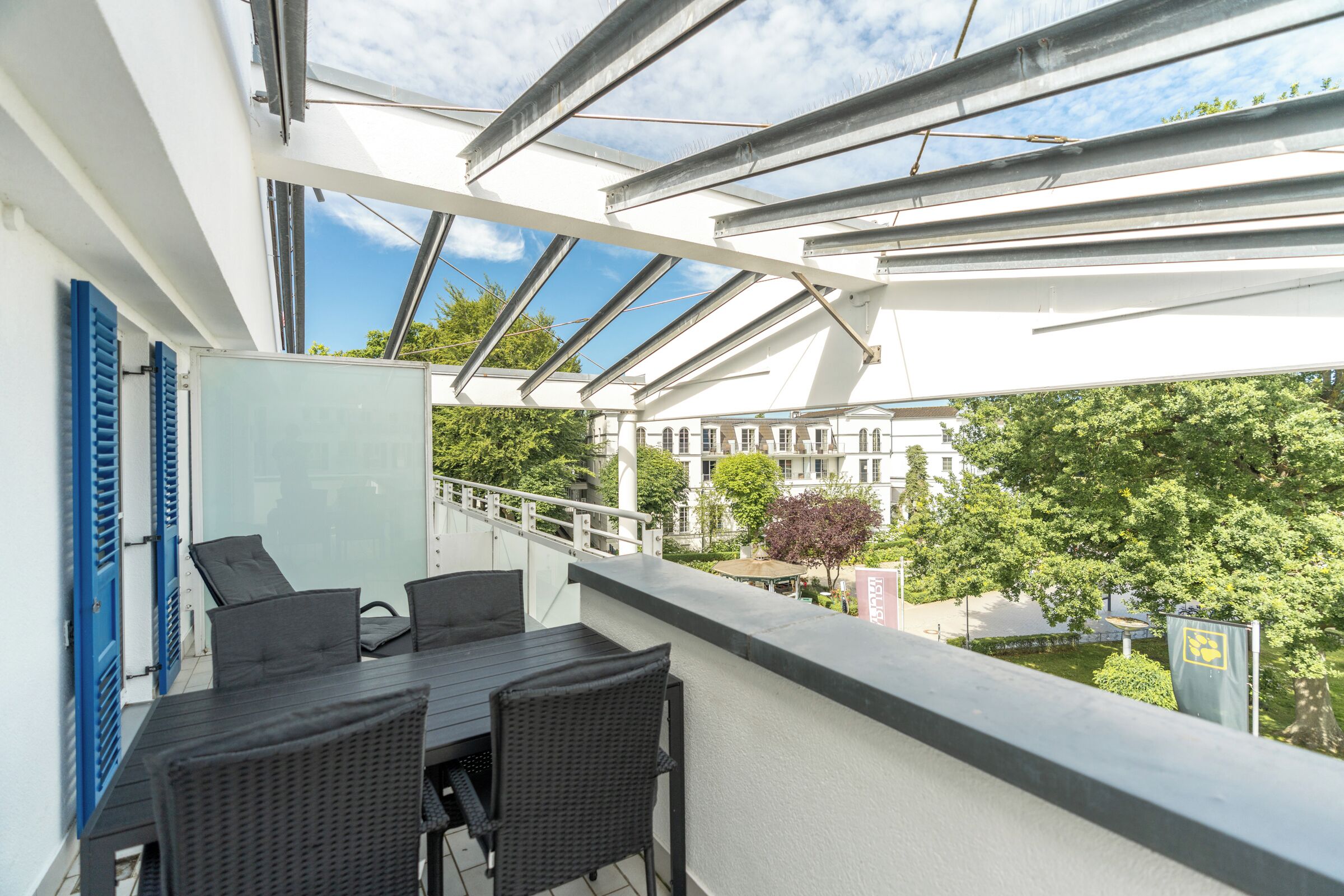 A balcony with a table and chairs, a view of a building, and a tree.