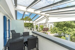 A balcony with a table and chairs, a view of a building, and a tree.