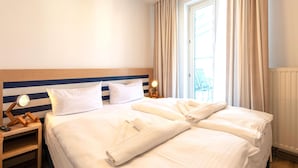 Une chambre d’hôtel avec deux lits, une table de chevet avec une lampe et une fenêtre avec des rideaux.