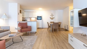 Un espace de vie compact comprenant un coin cuisine, un coin repas et un téléviseur fixé au mur.