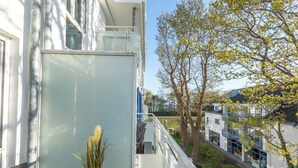 A balcony with a glass door, a potted plant, and a view of a building with balconies and trees.