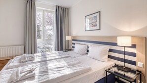 A hotel room with a bed, two bedside lamps, a framed picture on the wall, and a window with curtains.