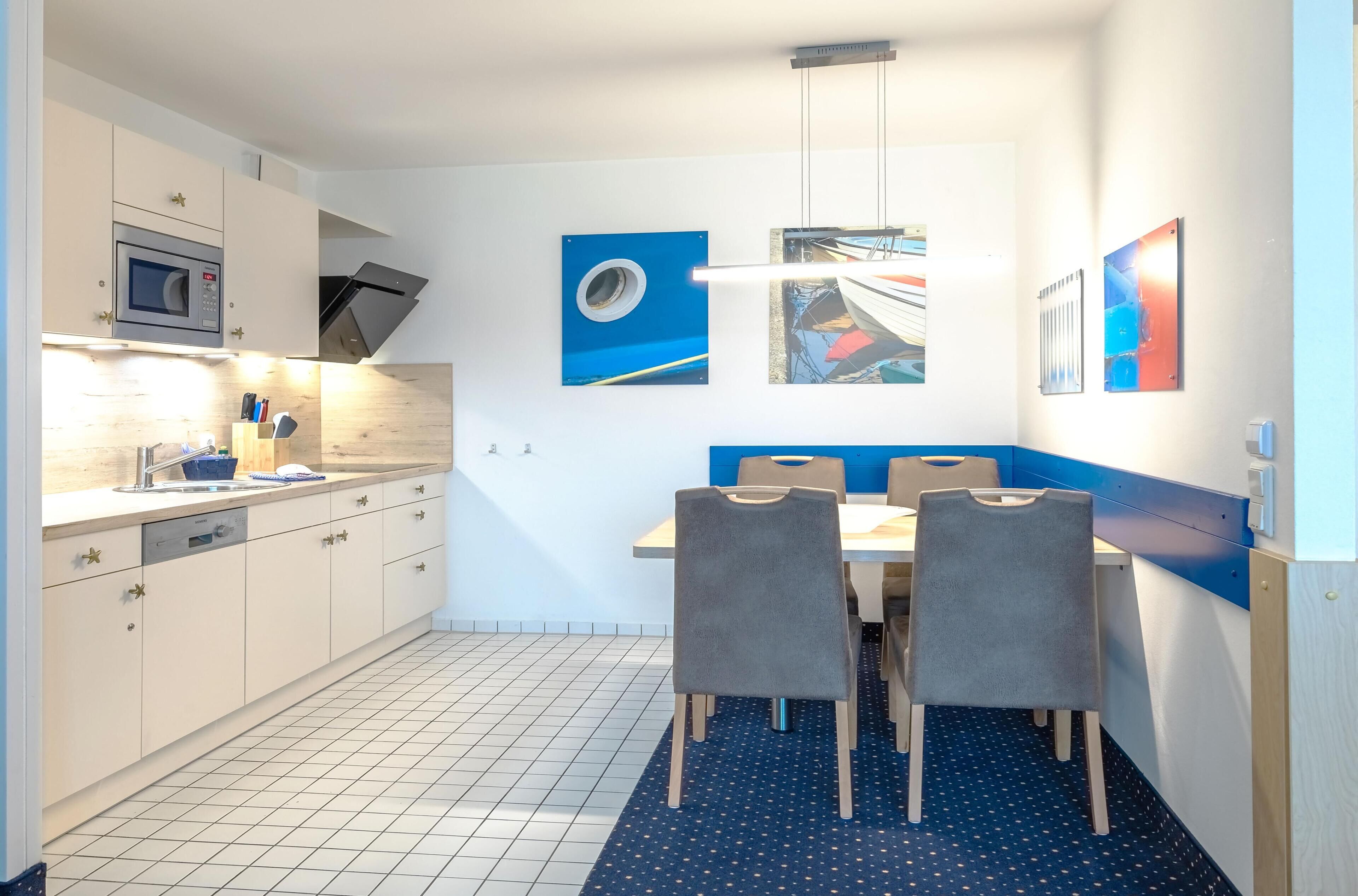 Una cocina moderna con armarios blancos, un microondas y un comedor con una pared azul de acento y dos sillas.