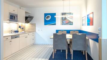 Una cocina moderna con armarios blancos, un microondas y un comedor con una pared azul de acento y dos sillas.