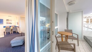Une chambre d’hôtel avec un balcon, un coin repas et un espace salon aménagé avec des meubles en osier.