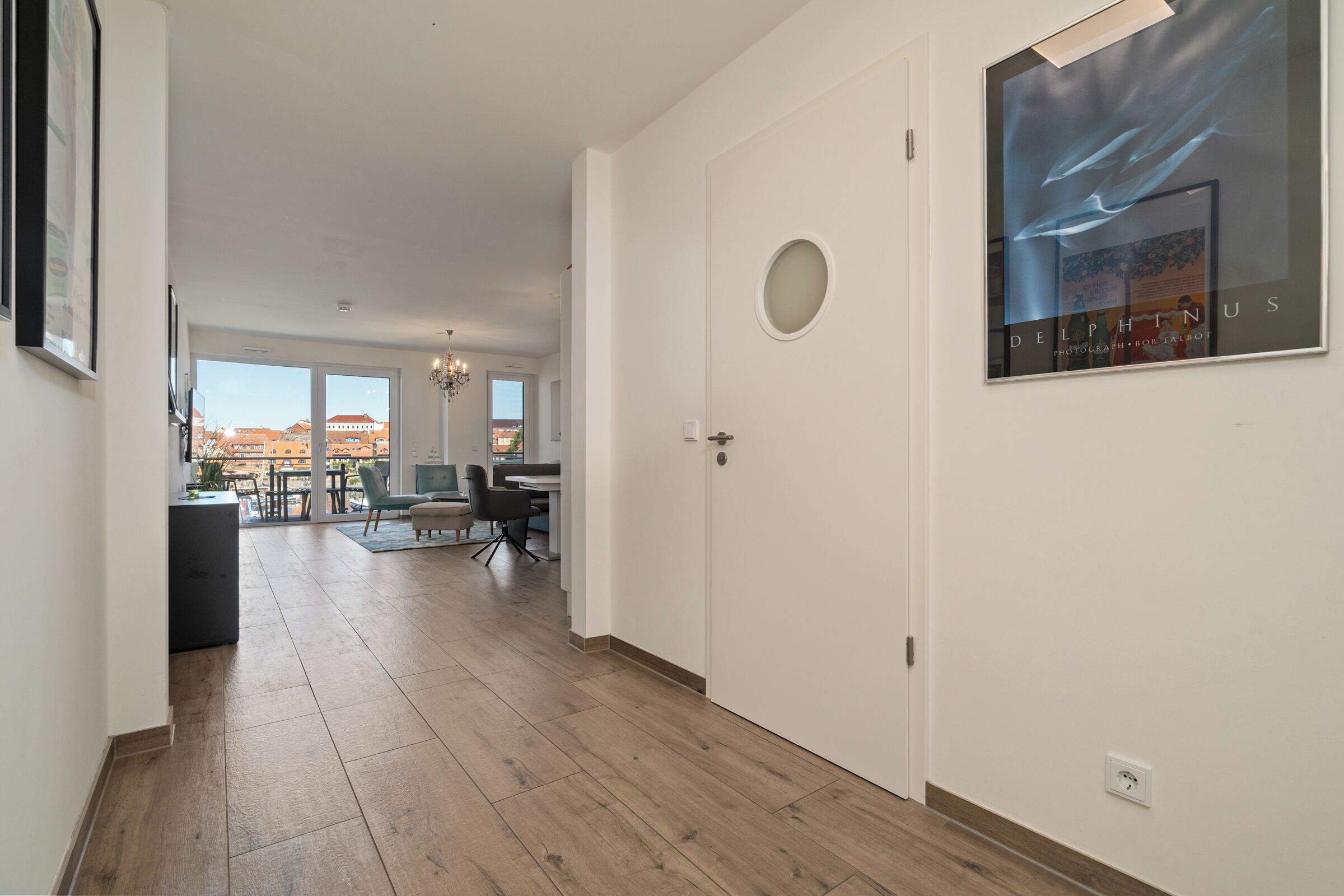 A spacious hallway with a wooden floor leading to a dining area with natural light and a view of buildings.