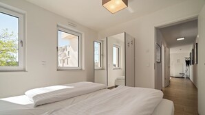 Une chambre moderne avec deux lits, de grandes fenêtres et un couloir menant à une salle de bain.