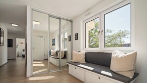 Une chambre moderne dotée d’une porte-fenêtre coulissante donnant sur une salle de bain, d’un banc intégré avec des coussins et d’une grande fenêtre offrant une vue sur les arbres.