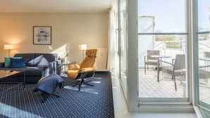 Ett modernt hotellrum med en soffa, en fåtölj och ett litet bord. Det finns en balkong med utemöbler.